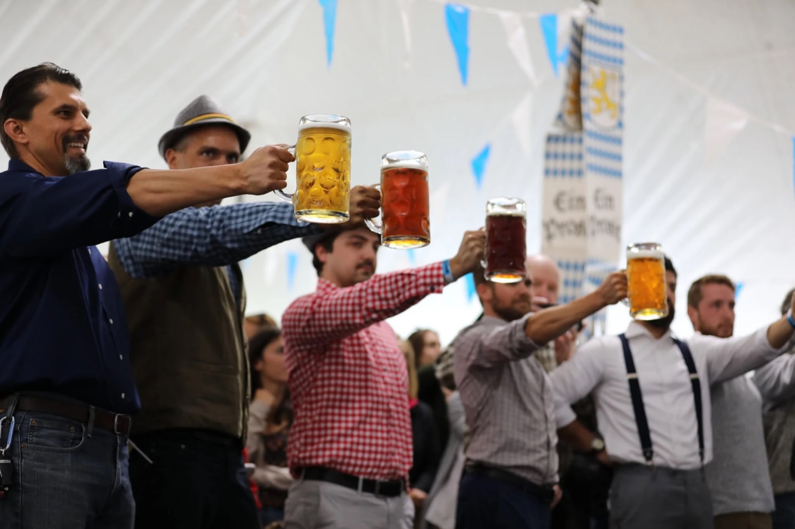 Men in the competition line holding steins of light and dark beer at arm's length under Bavarian bunting